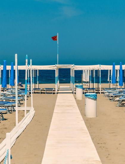 Spiaggia deserta con ombrelloni chiusi e mare sullo sfondo.